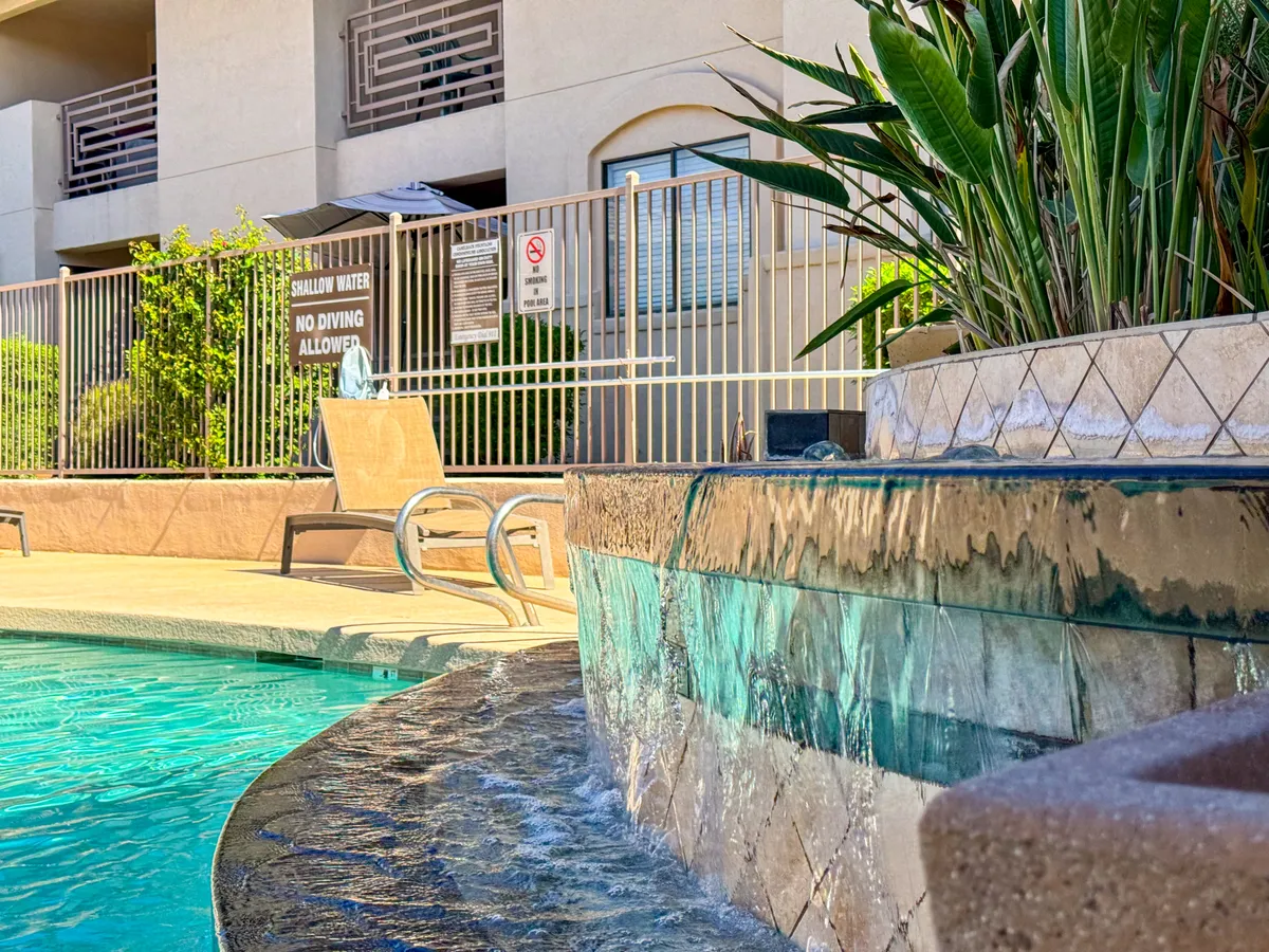 A serene exterior view of a sparkling swimming pool framed by lush green plants, inviting lounge chairs, and a gentle water feature. The area exudes a tranquil, resort-like ambiance perfect for unwinding after a productive workday.