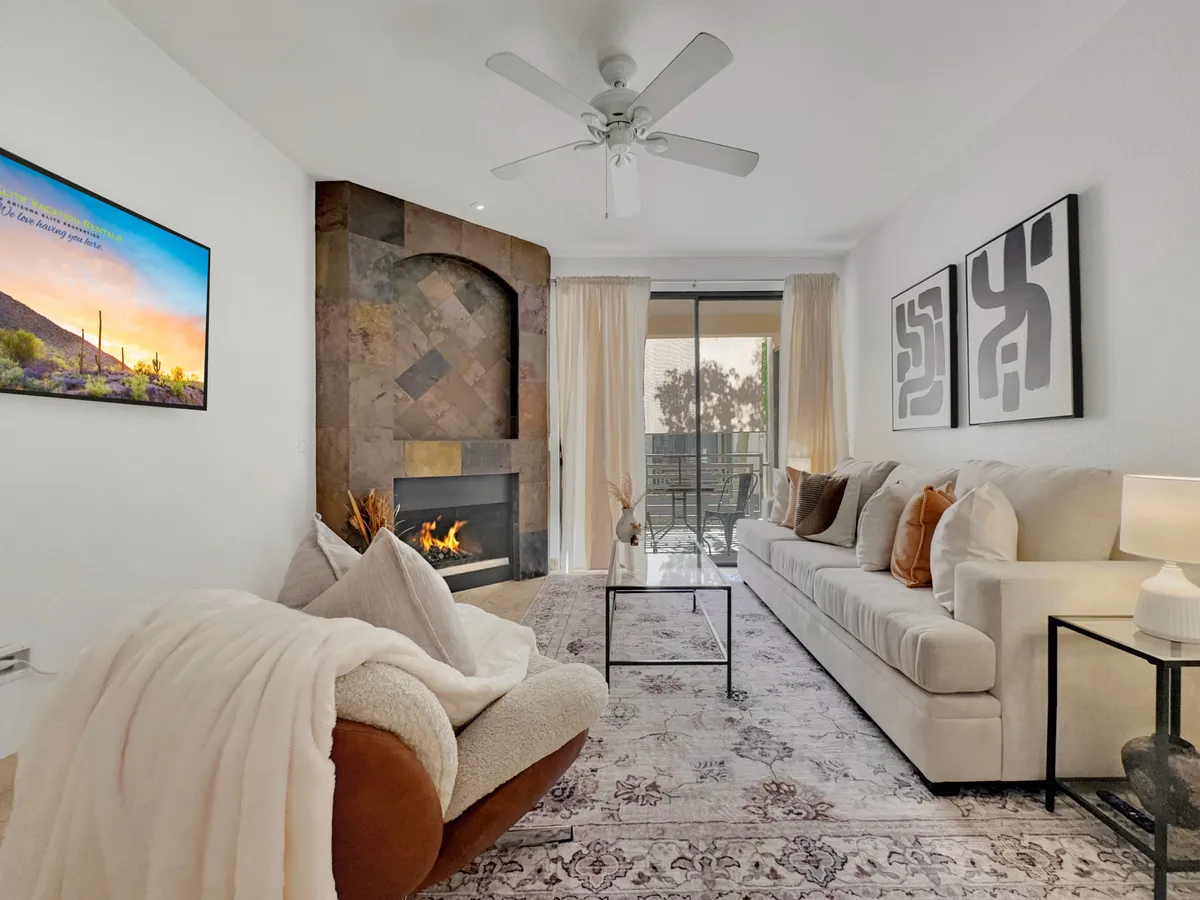 A sunken living room with a modern sofa, a stylish fireplace, contemporary artwork, a soft area rug, and a large television mounted on the wall. Warm lighting and plush textures create a cozy, inviting atmosphere, perfect for relaxing or socializing.