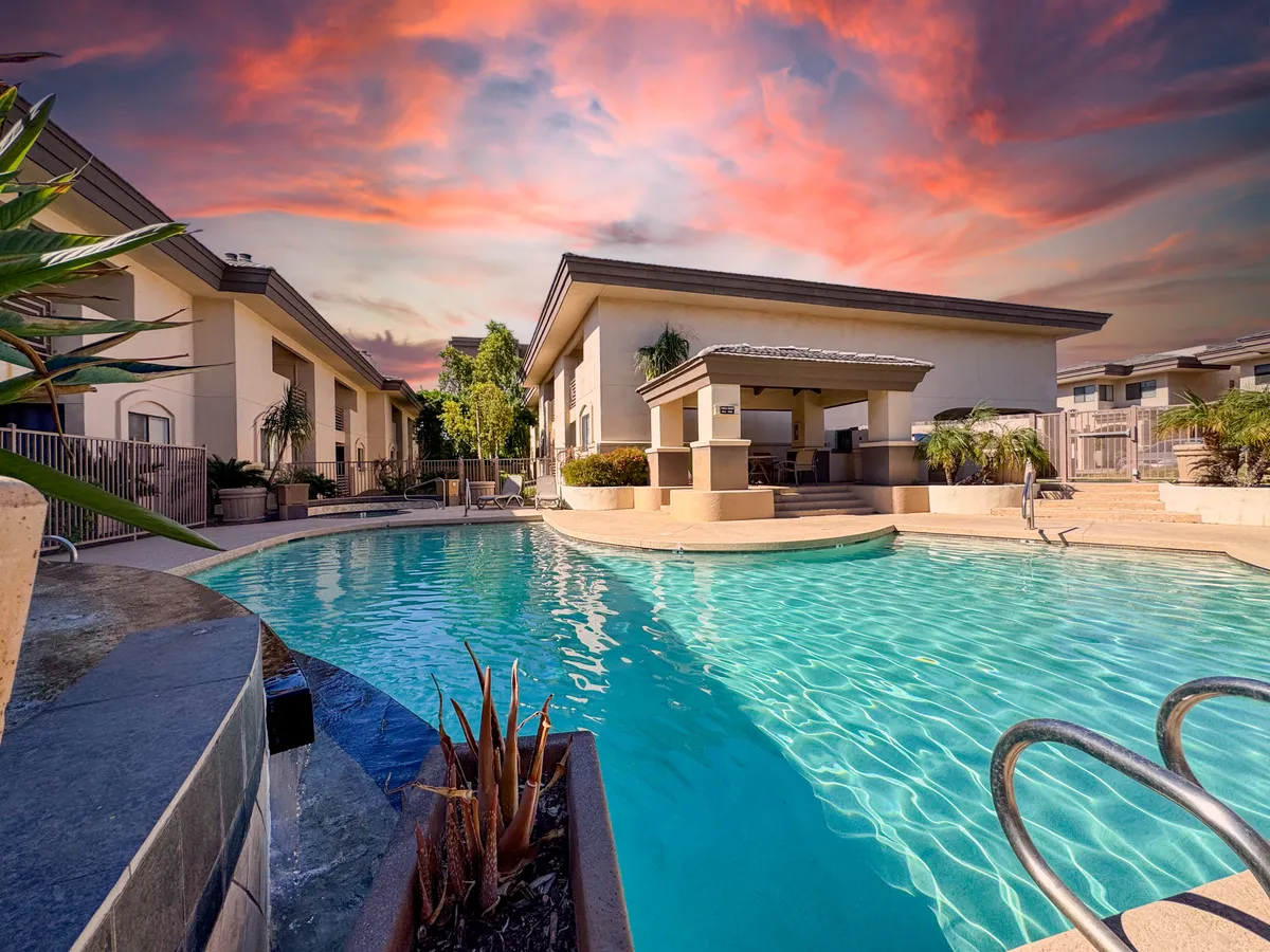 A year-round heated swimming pool surrounded by comfortable outdoor seating and lush greenery, set beneath a dramatic evening sky. The tranquil blue water glows in the soft twilight, with inviting lounge areas perfect for couples to unwind together after a day of exploring.