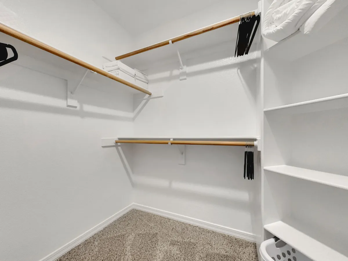 A tidy walk-in closet equipped with wooden hanging rods, shelves, and a laundry basket. The organized space is practical and offers ample room for storing clothes and planning outfits, reflecting ease of use and daily comfort.