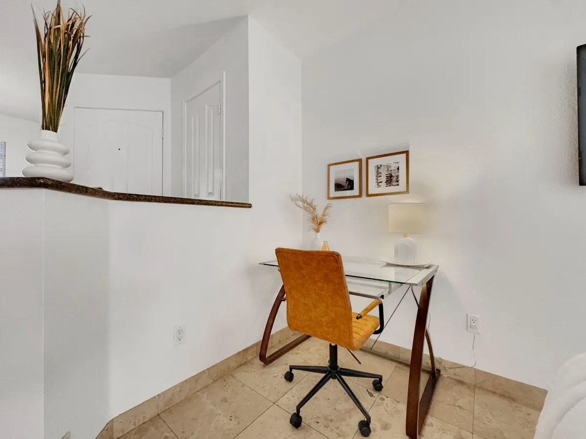 A modern, productive workspace featuring a glass desk paired with an orange chair. The setup includes a lamp, stylish artwork on the wall, and a decorative plant, creating a bright, focused area ideal for remote work or study.